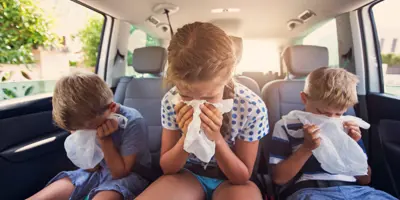 Drie kinderen zitten op de achterbank van een auto over plastic zakjes gebogen alsof ze moeten overgeven.