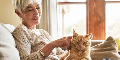 Lachende vrouw aait een roodharige kat op haar schoot op de bank.