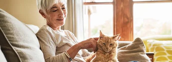 Lachende vrouw aait een roodharige kat op haar schoot op de bank.