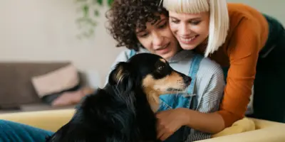 Twee vrouwen en een hond knuffelen op een mosterdgele bank.