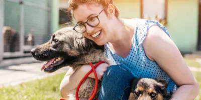 Een jonge vrouw hurkt en knuffelt haar hond in een zonnige tuin.