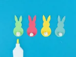Vier kartonnen konijntjes in groen, roze, geel en blauw waarop propjes wc-papier zijn geplakt als staartjes.
