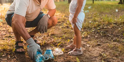 Opa leert peuter zwerfvuil te verzamelen in een zonovergoten park.
